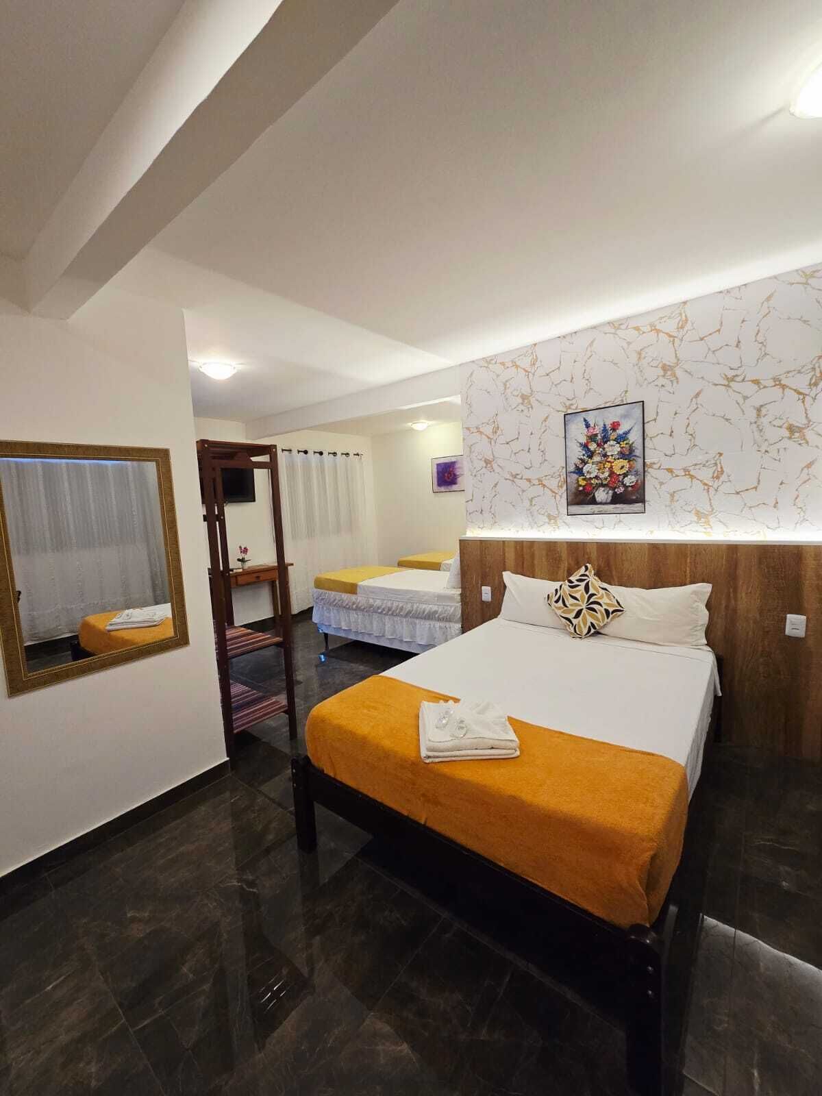 A hotel room with a large bed, a smaller bed, a mirror, a painting, and a wooden headboard.