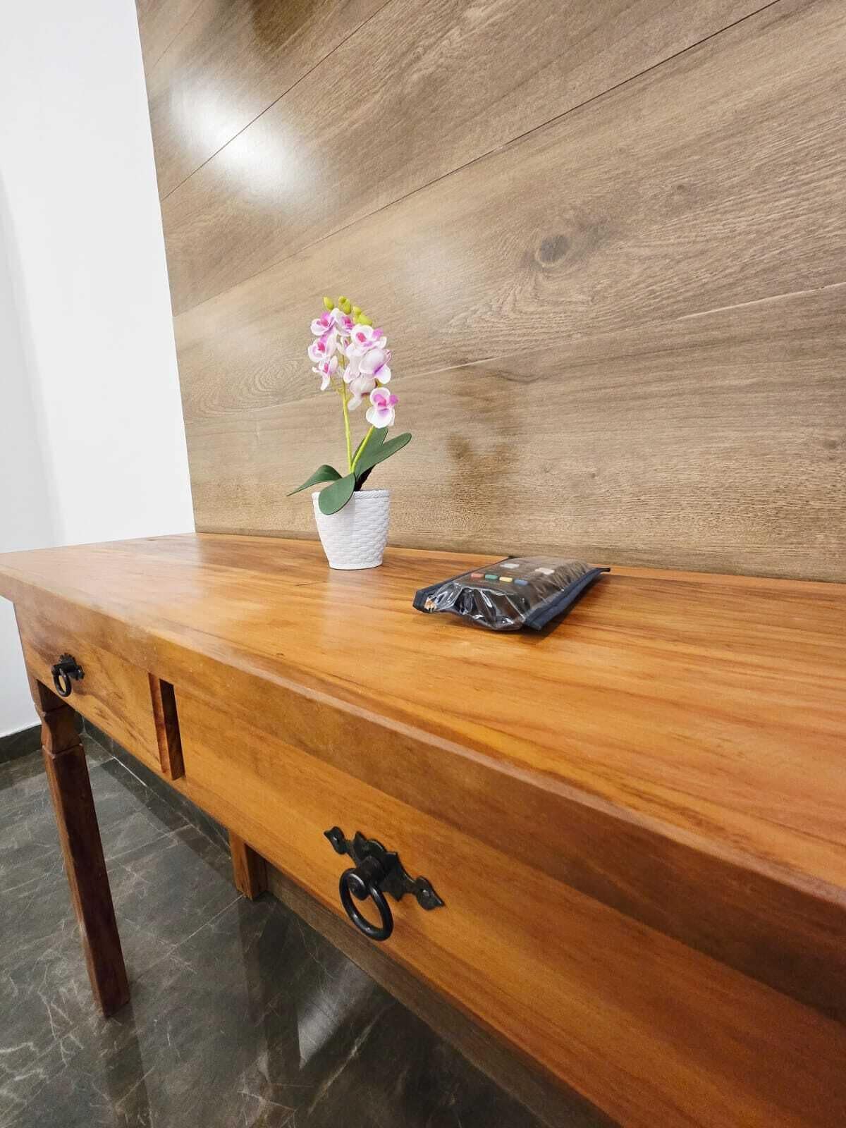 Escritorio de madera con una maceta blanca que contiene flores rosadas, una bolsa de plástico y un tirador negro tipo aro.