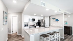 A modern kitchen with white cabinetry, stainless steel appliances, and a granite countertop. - Sandcastle Condominium Unit 329 (Port Aransas)