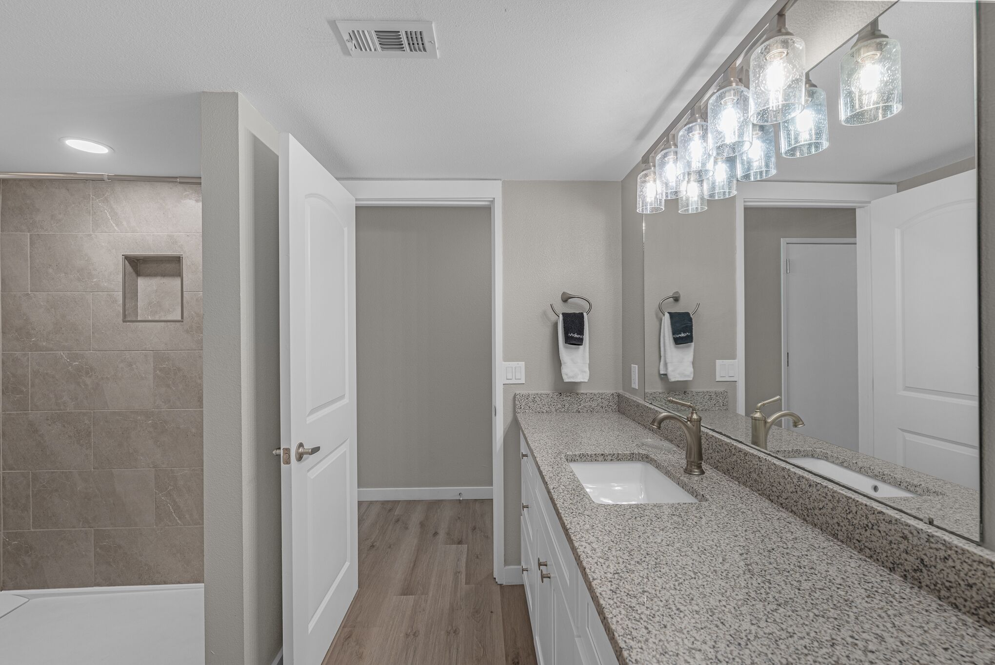 A modern bathroom with a granite countertop, a large mirror, and a shower area.