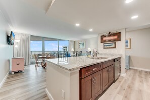 A modern kitchen with a large island, wooden cabinets, and a view to the outside. - Sandcastle Condominium Unit 413 (Port Aransas)