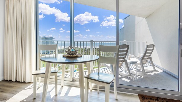 En balkon med et bord og stole, havudsigt og et hvidt gelænder.