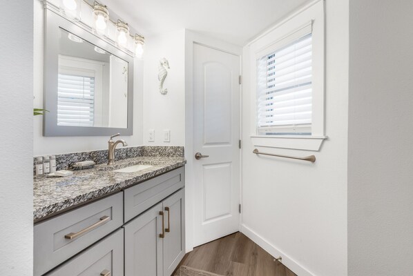 A bathroom with a granite countertop, a white door, and a window with blinds. - Sandcastle Condominium Unit 426 (Port Aransas)