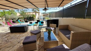 Un patio al aire libre con mobiliario de mimbre, una mesa con cubierta de vidrio y una piscina al fondo.