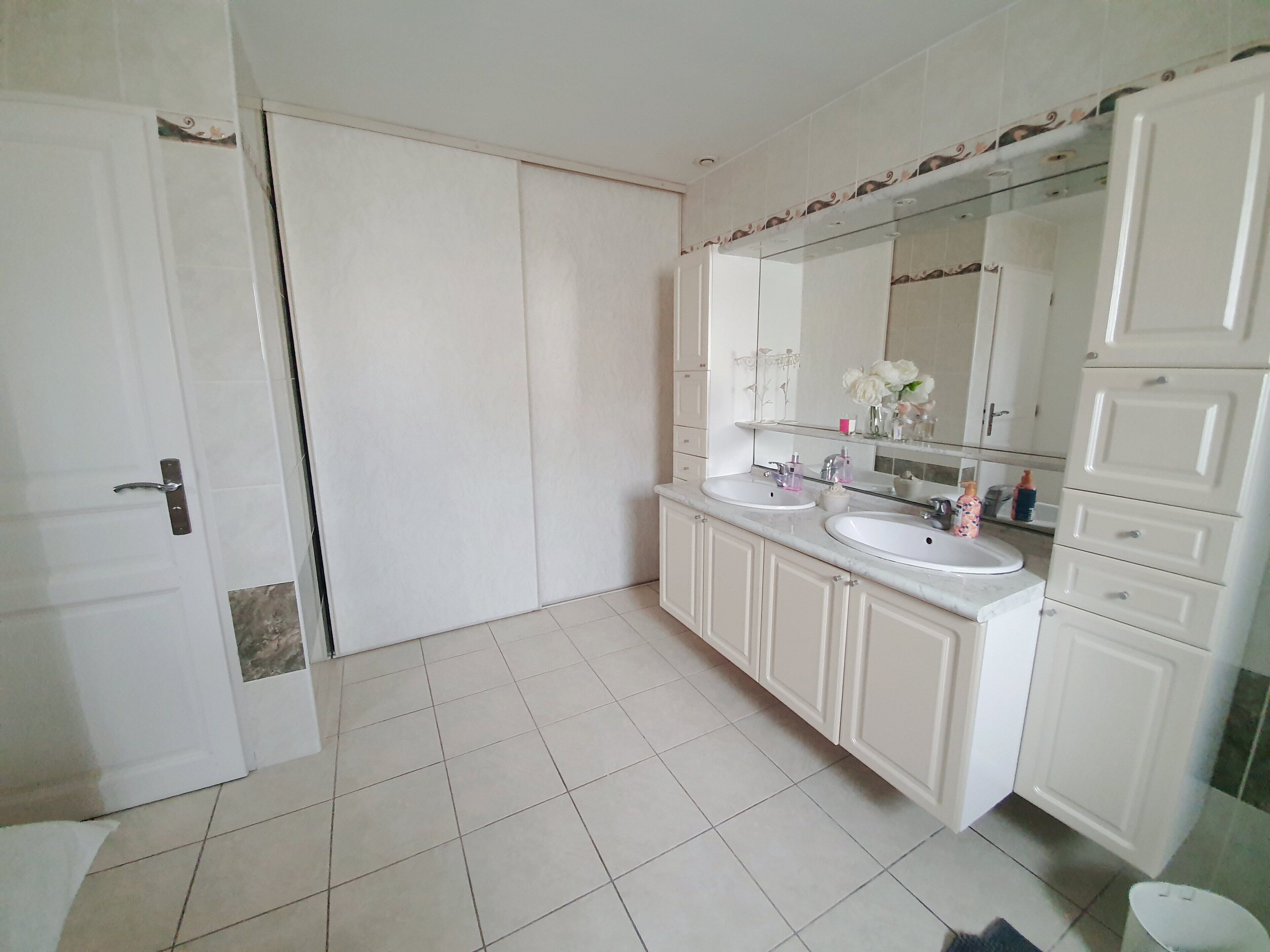 Une salle de bain avec deux lavabos, un grand miroir et des meubles blancs.