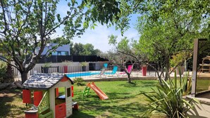 Un patio trasero con una casita de juegos, un tobogán y una piscina.