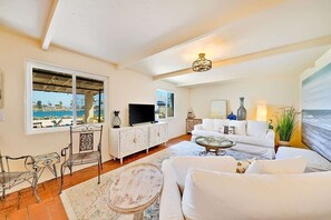 Un salon avec un téléviseur, un canapé blanc et une vue sur la mer.