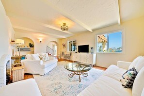 A living room with white sofas, a glass coffee table, and a TV on a white cabinet.