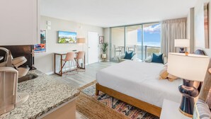 Une chambre d’hôtel avec un grand lit, un bureau avec une chaise, une télévision et un balcon donnant sur la mer.