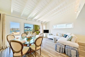 A modern living room with a glass dining table, a white sofa, and a TV.