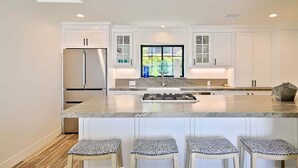 Une cuisine moderne avec des meubles blancs, un îlot central doté de tabourets et une grande fenêtre.
