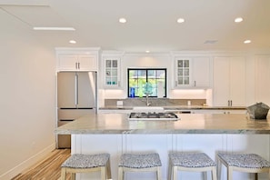 A modern kitchen with white cabinetry, a central island with stools, and a large window.