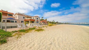 Une propriété située en bord de mer, avec une plage de sable, une clôture et plusieurs maisons aux toits recouverts de tuiles rouges.