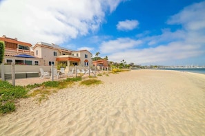 A beachfront property with a sandy beach, a fence, and several houses with red-tiled roofs.