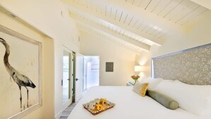 Une chambre d’hôtel avec un grand lit, un tableau représentant un oiseau, un plateau avec des tasses et une fleur, et une vue sur l’extérieur.