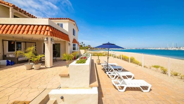 A hotel with a terrace, lounge chairs, and a view of the sea. - On The Beach Clubhouse - Bayfront beauty (San Diego)