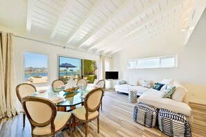 A modern living room with a glass dining table, a white sofa, and a TV.