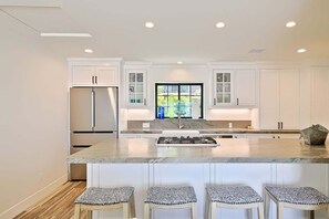 A modern kitchen with white cabinetry, a central island with stools, and a large window.