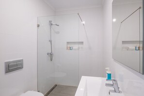 Un baño moderno con cabina de ducha de vidrio, un lavabo blanco y un espejo.