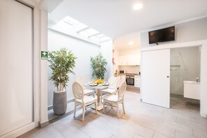 Una cocina moderna con armarios blancos, un televisor de pantalla plana sobre la encimera y una zona de comedor con mesa y sillas.