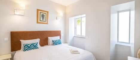 Un dormitorio con una cama grande, cabecera de madera, dos mesitas de noche, una silla y una ventana.