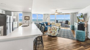 A modern kitchen with a large island, a dining area with a view, and a living room with a sofa and ottoman. - Sandcastle Condominium Unit 438 (Port Aransas)