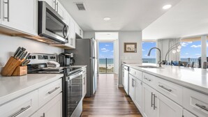 A modern kitchen with white cabinets, stainless steel appliances, and a wooden floor. - Sandcastle Condominium Unit 438 (Port Aransas)