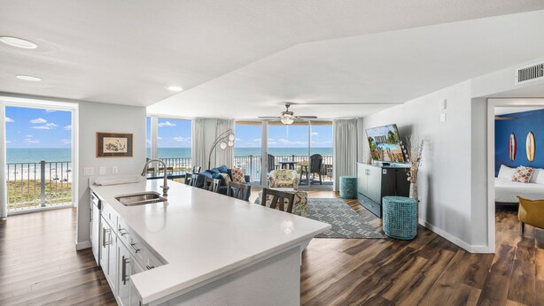 A spacious living area with a large island, a dining table, and a view of the ocean. - Sandcastle Condominium Unit 438 (Port Aransas)