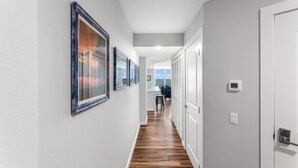 A hallway with framed pictures on the wall, a wooden floor, and a view to a dining area. - Sandcastle Condominium Unit 438 (Port Aransas)