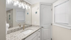 A bathroom with a granite countertop sink, a large mirror, and a door with a window. - Sandcastle Condominium Unit 506 (Port Aransas)