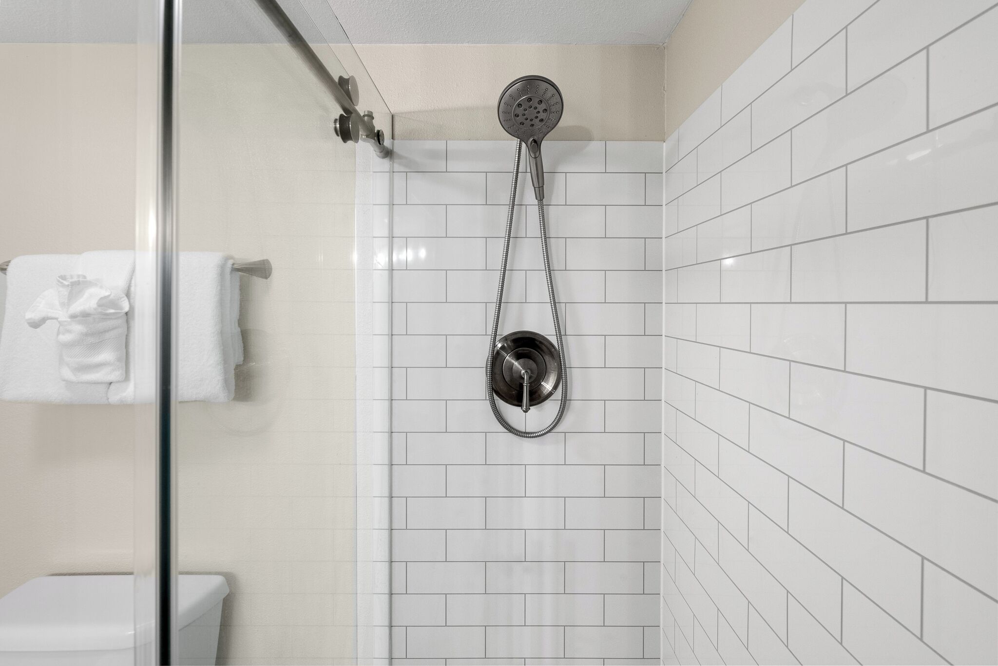 Une salle de bain avec des murs recouverts de carreaux blancs, une douche en verre et des toilettes blanches.
