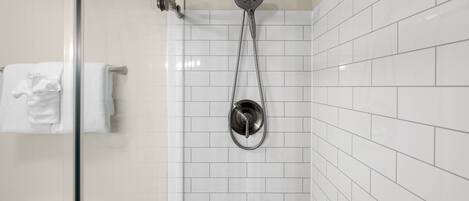 Une salle de bain avec des murs recouverts de carreaux blancs, une douche en verre et des toilettes blanches.