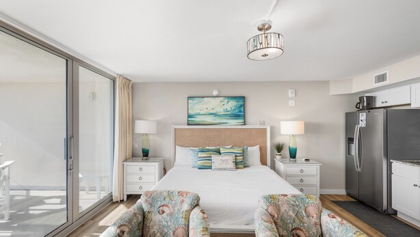 A bedroom with a bed, two nightstands, a dresser, and a large window. - Sandcastle Condominium Unit 506 (Port Aransas)