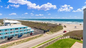 Un motel à plusieurs étages avec un parking, offrant une vue sur une plage et l’océan.