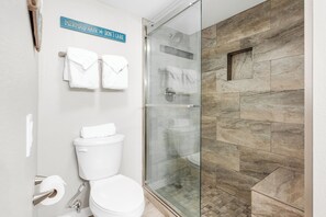 A bathroom with a glass-enclosed shower, a toilet, and a sign indicating a hair care service. - Sandcastle Condominium Unit 526 (Port Aransas)