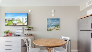 A modern kitchen with a wooden dining table, white chairs, a built-in refrigerator, and artwork on the walls.