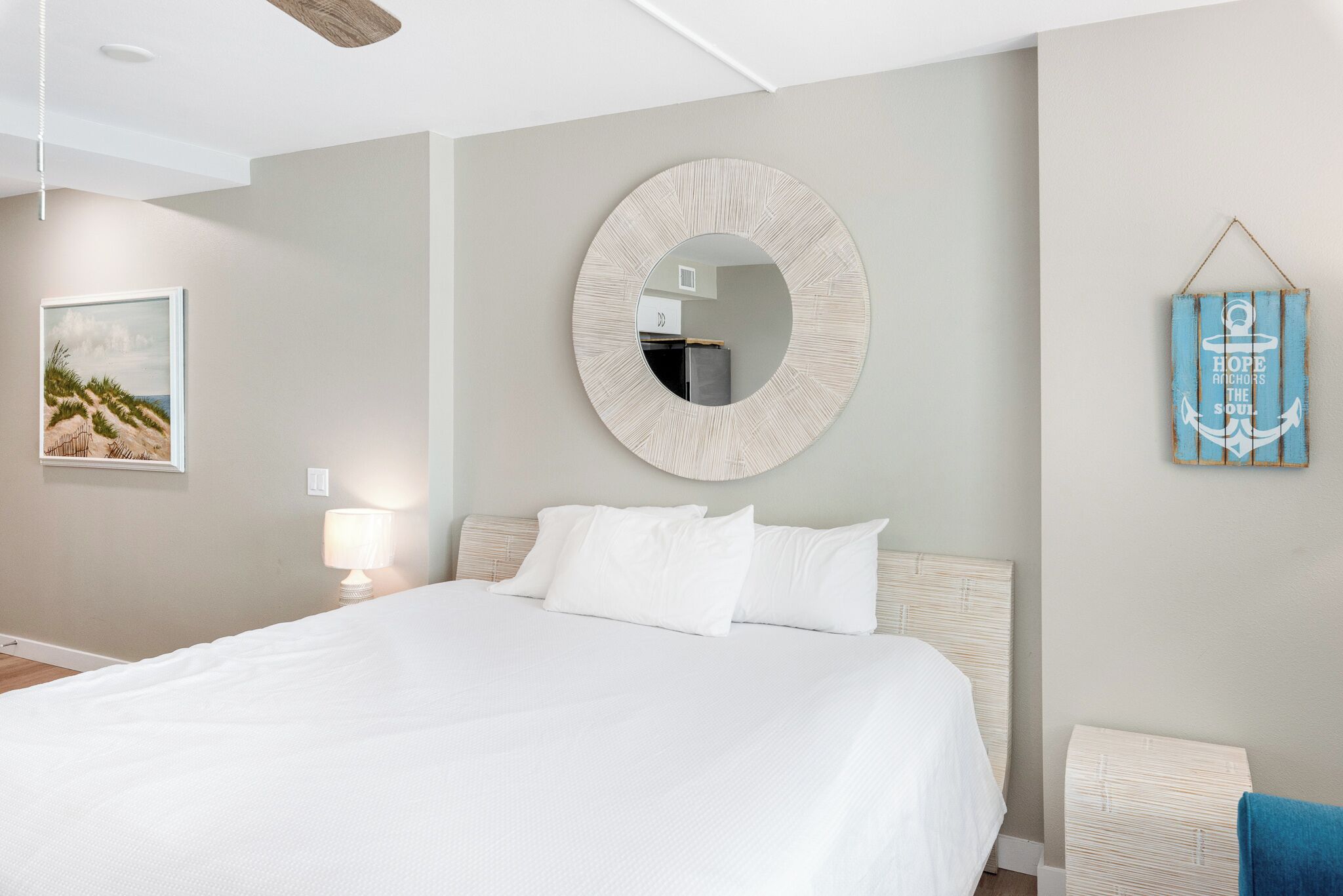 Een slaapkamer met een groot bed, een ronde spiegel, een lijst met een foto, een bedlamp en een blauw bord aan de muur.