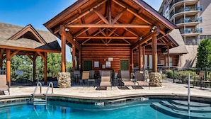 A wooden poolside area with lounge chairs and a covered seating area.