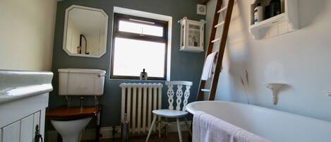Un baño con inodoro, radiador, ventana, bañera y un estante con artículos de aseo.
