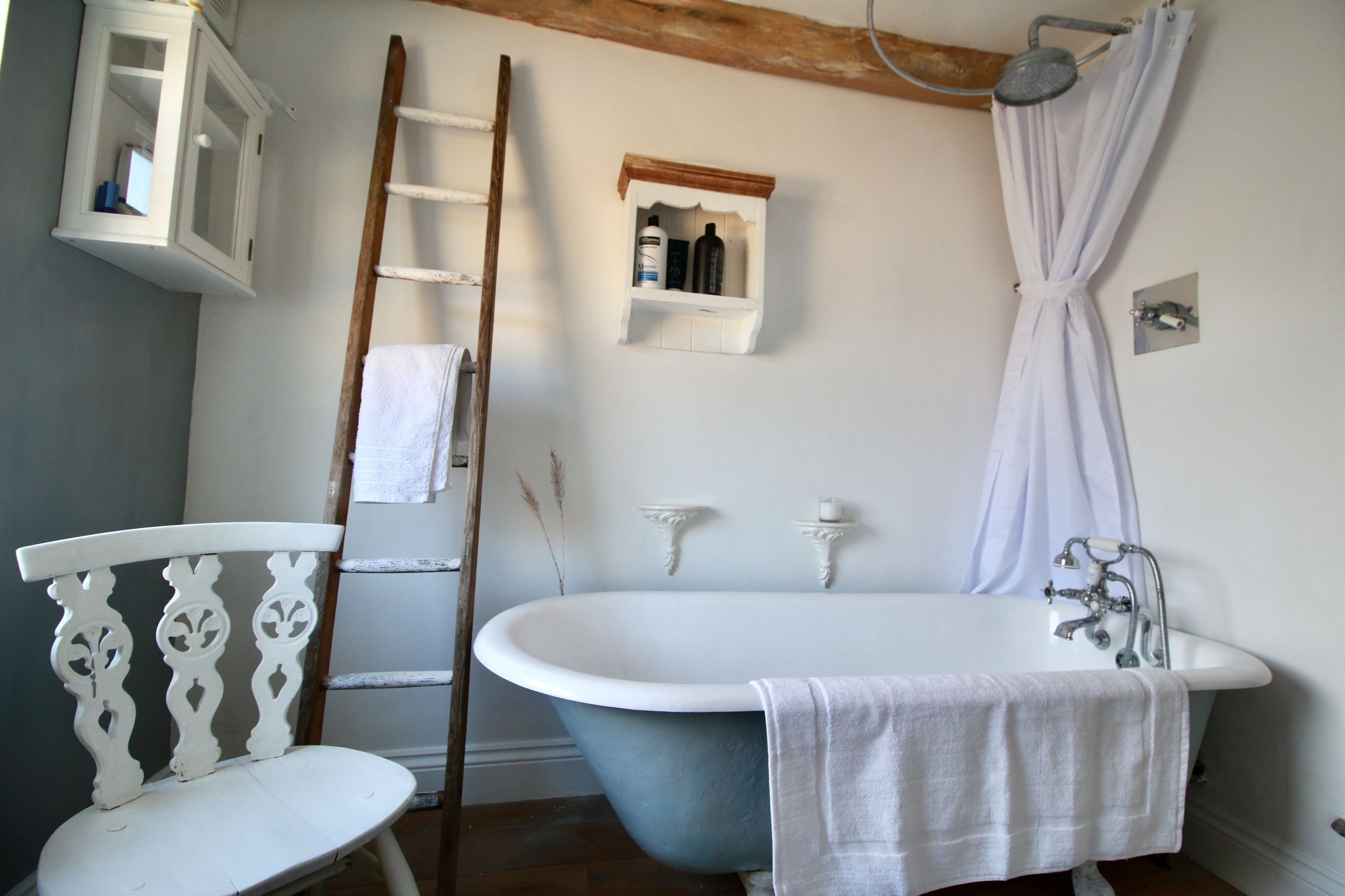 A bathroom with a clawfoot bathtub, a wooden chair, a ladder, a cabinet, and a shower curtain.