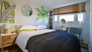 Een slaapkamer met een bed, nachtkastjes, een spiegel, een raam met zonwering en een kamerplant.