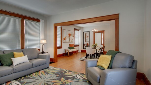 Una sala de estar con un sofá gris, un sillón azul y un comedor con mesa y sillas.