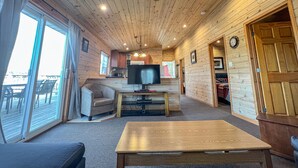 Een knus interieur van een chalet met een houten plafond, een plafondventilator, een televisie, een bank, een bijzettafeltje en een schuifdeur die leidt naar een terras.
