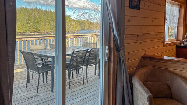 Een houten chalet van binnen met een schuifdeur naar een terras buiten, met een tafel en stoelen.
