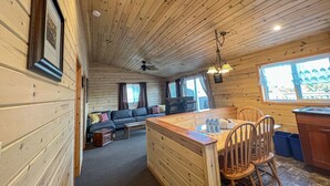 Een gezellig cabin interieur met houten plafond, een bank, een eettafel met stoelen en een keukenhoek.