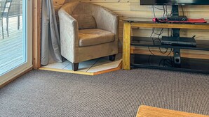 Een gezellig houten interieur met een comfortabele fauteuil, een flatscreen-televisie en een klein keukentje.