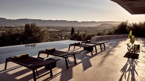 Una piscina infinita con sillones de descanso y vistas a montañas distantes.