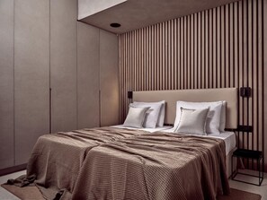 Quarto moderno com uma cama grande, cabeceira com ripas verticais e uma pequena mesa de cabeceira.