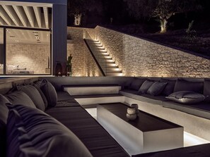 Uma área externa moderna para relaxamento, com parede de pedra, sofá embutido e mesa de centro.