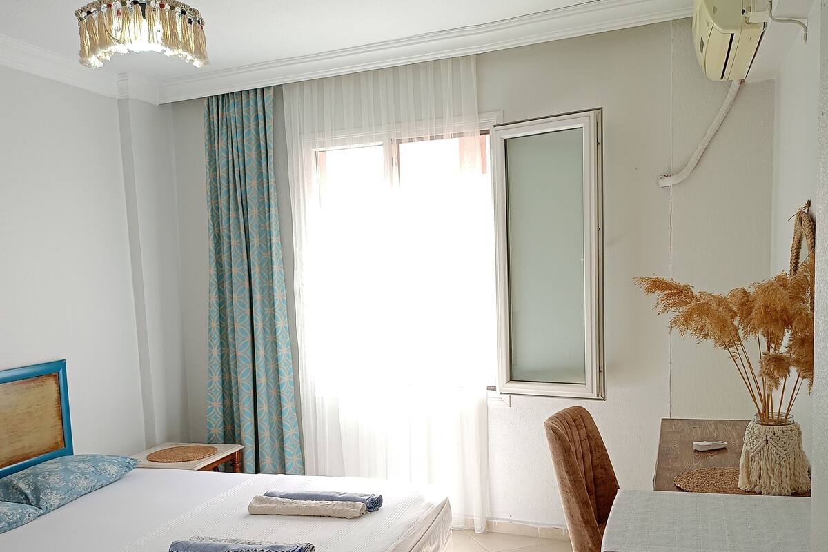 A bedroom with a bed, a desk, a chair, a radiator, and a window with curtains.